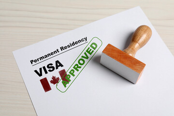 Document with approved permanent residency visa in Canada and stamp on white wooden table - obrazy, fototapety, plakaty