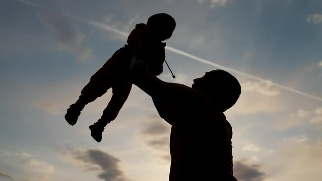 Happy family walks in park outdoors. Father and son silhouette. Parent father throws child into air at sunset. Happy child in hands of his father in park at sunset. Family walking outdoors in the park
