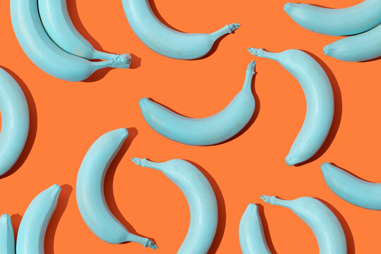 Creative pattern made with pastel blue bananas on bright orange background. 80s, 90s retro aesthetic style romantic concept. Minimal fashion surreal fruit idea.