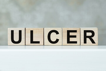 Stomach ulcer symbol. Wooden cubes with the word ulcer. On the table. Beautiful brick background. Medicine and stomach ulcer concept.