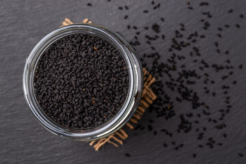 Glass jar full of black cumin seeds over black background. Macro. Cooking with nigella seeds concept. Kalonji as spice and seasoning. Nigella sativa for Ayurveda herbal medicine.