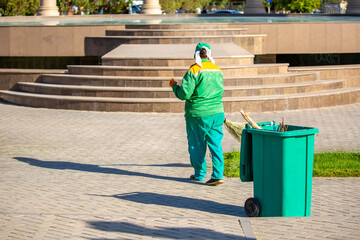 The janitor cleans the city street with a broom in the city. Street cleaning service. A worker...