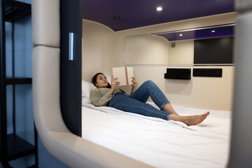 Young woman reading book in capsule of pod hostel