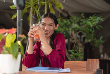 A happy trans woman smiles for the camera as she enjoys her sunny morning with a cold juice at an al fresco cafe.
