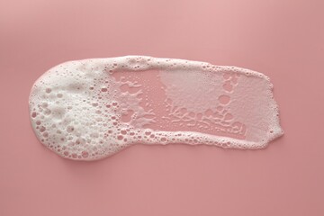 Smudge of white washing foam on pale pink background, top view