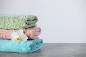 Obraz na płótnie Canvas Stacked soft colorful towels with flower on grey table, space for text