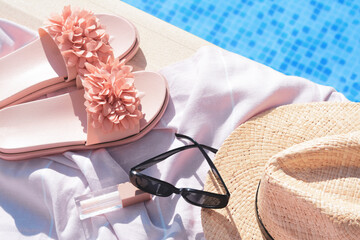Pink blanket with beach accessories near outdoor swimming pool on sunny day, above view