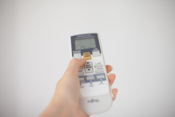holding remote control for air conditioning at home. Using air conditioning system for warming...