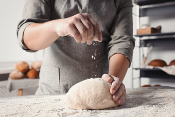 Man sprinkling flour over dough at table in kitchen, closeup