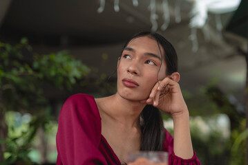 A sad looking trans woman sitting outside rests her head on her knuckles as she looks up and frowns while thinking about her problems. - obrazy, fototapety, plakaty