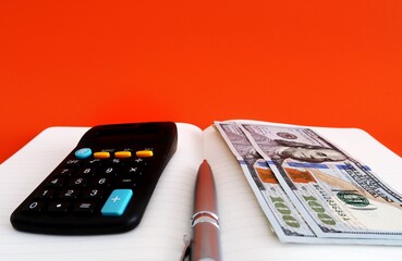 Black calculator, dollars cash money, pen on open notebook, isolated on orange background. Concept...