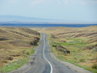 Empty road towards the horizon with mountains and clouds in the background