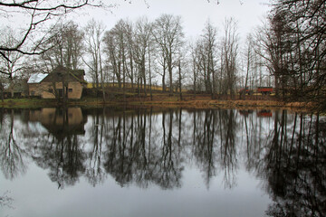 View on the small house and naked trees reflecting in a lake. Selective focus