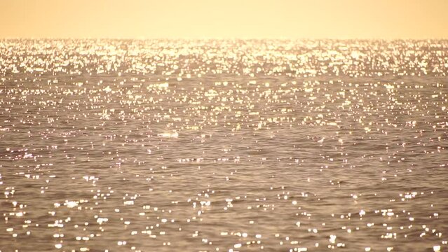 Abstract aerial sea summer ocean sunset nature background. Small waves on azure water surface in motion blur with golden bokeh lights from sun. Holiday, vacation and recreational concept. Slow motion