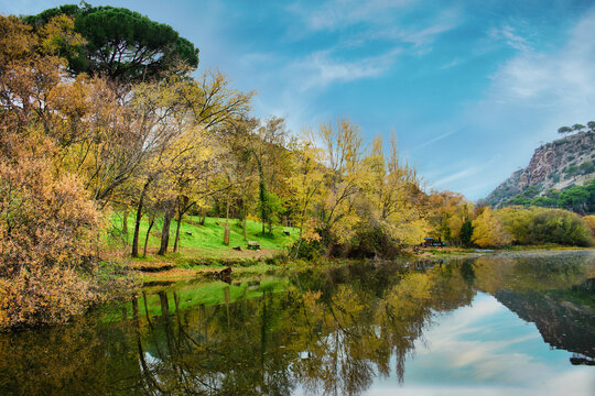 Autumnal view of the banks of the Alberche River, in the the Picadas reservoir, Madrid, Spain, with reflection of trees and cloudy sky in water.