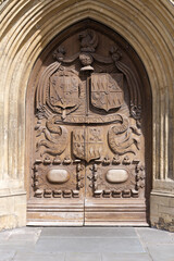 Entrance with decorated wooden door of famous Abbey Church of Saint Peter and Saint Paul at City of Bath on a blue cloudy summer day. Photo taken August 2nd, 2022, Bath, United Kingdom.