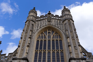 Main entrance of famous Abbey Church of Saint Peter and Saint Paul at City of Bath with angels climbing ladder on a blue cloudy summer day. Photo taken August 2nd, 2022, Bath, United Kingdom.