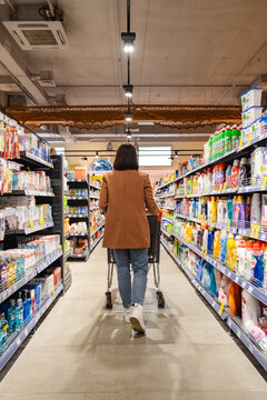 a woman with a cart walks between rows of shelves in a grocery store