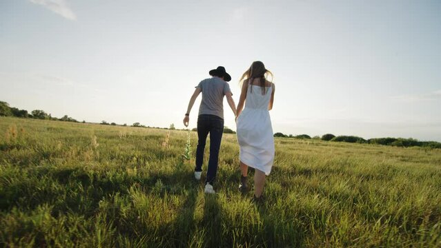 Couple walks across green field joining hands at sunset