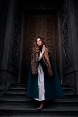 Fairytale princess wearing cloak with medieval castle door on the background.