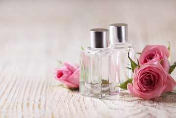 Bottles of essential oils and roses on white wooden table, space for text