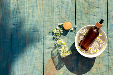 Bottle of chamomile essential oil and flowers on light blue wooden table, flat lay. Space for text