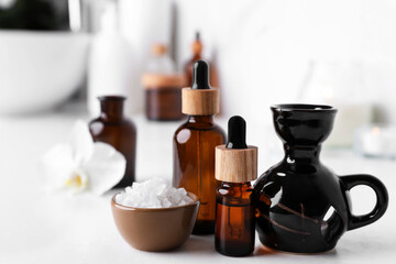 Obraz na płótnie Canvas Essential oils, sea salt and aroma lamp on white table in bathroom, closeup. Space for text