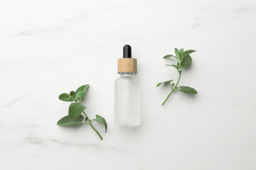 Fototapeta na wymiar Bottle of mint essential oil and fresh herb on white marble table, flat lay