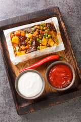 Turkish kebab with vegetables in parchment, accompanied by sauces close-up on a wooden tray on the table. Vertical top view from above