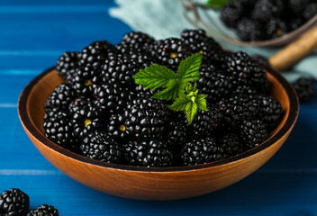 Bowl with fresh ripe blackberries on blue wooden table, closeup