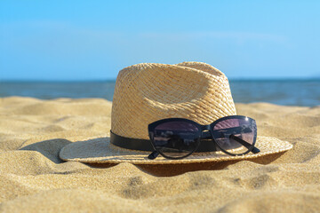 Hat with beautiful sunglasses on sand near sea