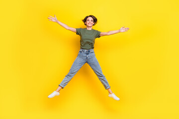 Fototapeta na wymiar Full size photo of nice adorable cheerful girl bob hairstyle wear khaki t-shirt denim jeans flying isolated on yellow color background