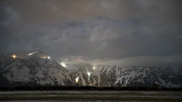 Time Lapse Lockdown Shot Of Lights Moving On Snowy Mountain Range By Forest At Night - Jackson, Wyoming