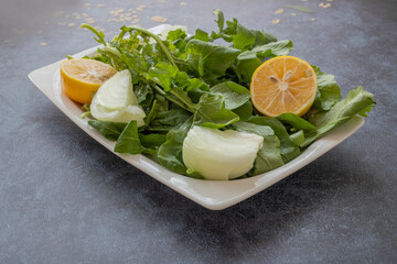 Fresh arugula salad in a white plate on a gray stone background .