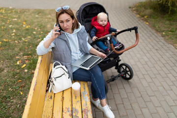 a woman with a stroller with a child talking on the phone Sitting on a bench while walking in the park