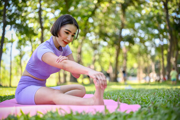 Naklejka na ściany i meble Fit Asian female in sportswear stretching her leg, warming up before workout in park.