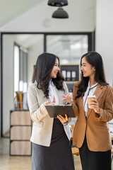 Two young female business colleagues smiling and discussing financial numbers and calculations and relaxing coffee at the office.