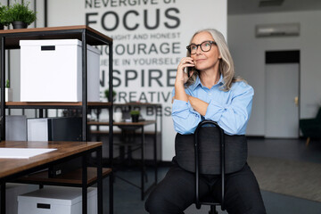top manager Middle aged older business woman sits on a chair and speaks on a mobile phone, work...