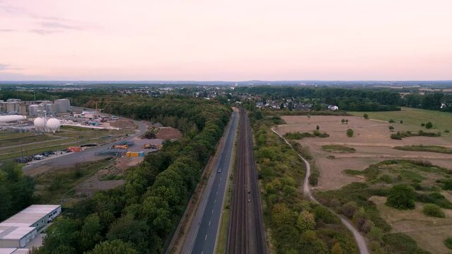 Aerial drone flight along train tram tracks in south of Cologne, Köln Sürth, Germany - bird view - flyover street train tram tracks forest and fields in summer 2022