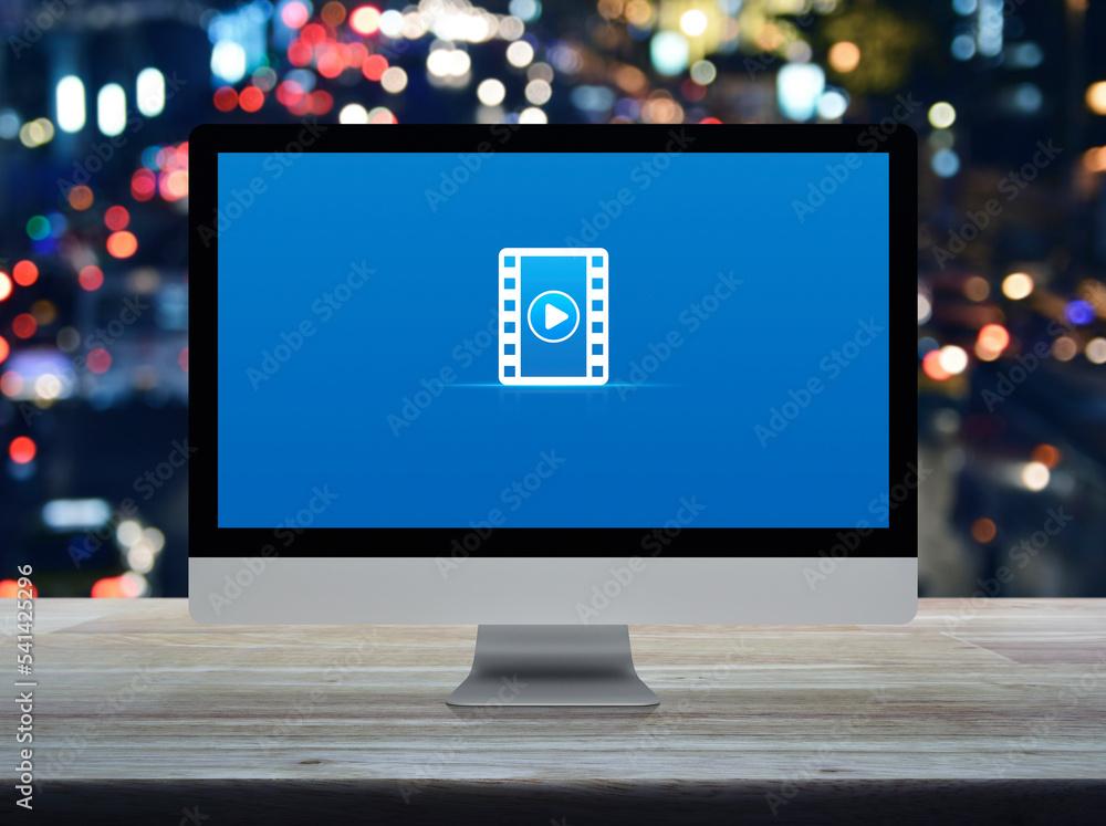 Poster play button with movie flat icon on desktop modern computer monitor screen on wooden table over blur