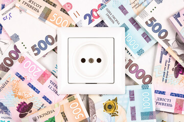 White socket over UAH banknotes hryvnyas as background. Concept of increasing prices for electricity in Ukraine. High energy cost