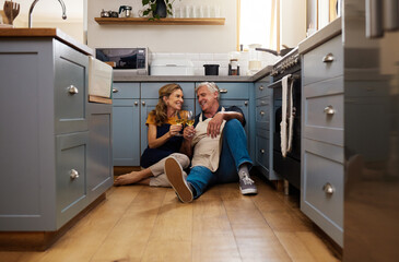 Couple, senior and wine in kitchen, floor and wood for romance, bonding or love in home for happiness. Elderly, man and woman make toast, happy or smile for glass, drinking and together on flooring