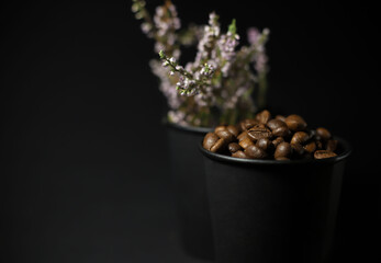 fragrant brown coffee beans with a slide next to purple flowers are poured in a black craft glass on a black background. for cafe menu signage labels splash screens
