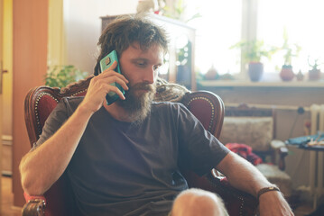 Reggae hippie man sitting in his living room, having a chat on his cell phone, sitting in a nice...