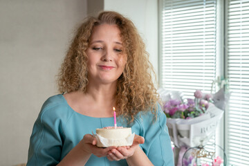 a middle-aged woman with a bento cake in her hands makes a wish and blows out a candle