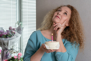 a middle-aged woman with a bento cake in her hands makes a wish and blows out a candle