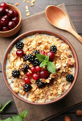Bowl of muesli served with berries and milk on wooden table, flat lay