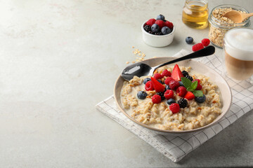Bowl of oatmeal porridge served with berries on light grey table, space for text