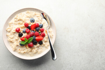 Bowl of oatmeal porridge served with berries on light grey table, top view. Space for text