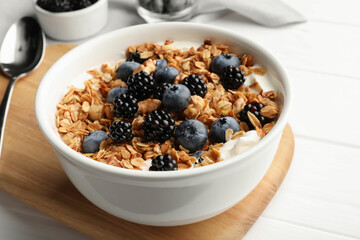 Bowl of healthy muesli served with berries on white wooden table, closeup